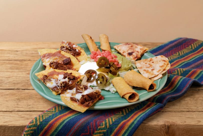 A platter of nachos, taquitos, and quesadillas with guacamole, sour cream, and jalapeños.