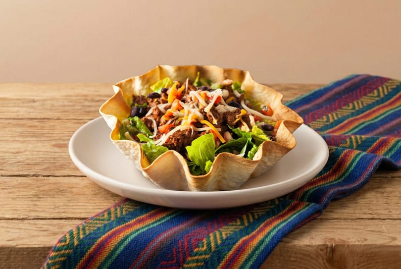 Taco salad in a crispy tortilla bowl with ground beef, lettuce, cheese, and beans.