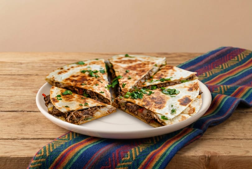Savory quesadillas filled with meat and cheese, garnished with parsley, on a white plate and colorful cloth.